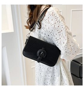 Detail of black patchwork shoulder bag featuring woven texture and round buckle