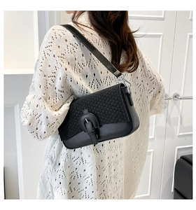 Model wearing a black woven leather shoulder bag with a vintage buckle detail