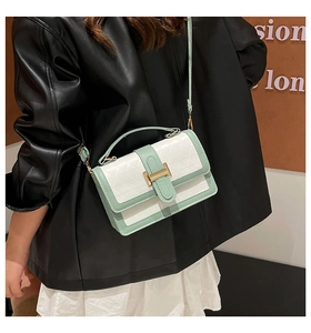 Detail of a white crossbody bag with green trim and geometric quilting on a model