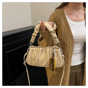 Detail of beige ruched cloud bag with adjustable strap and wooden bead tassel ornament