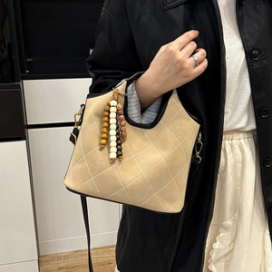 Quilted beige bucket bag with wooden beads tassel and black trim on a model