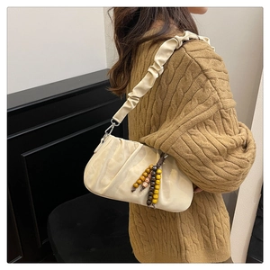 Close-up of beige pleated dumpling bag featuring colorful wooden bead charm and strap detail