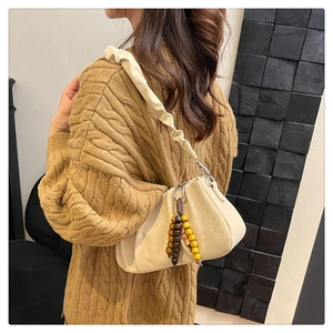 Close-up of pleated shoulder strap and wooden bead charm on cream faux leather hobo bag