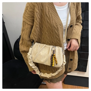 Detail of beige pleated cloud bag featuring retro wooden beads and textured leather