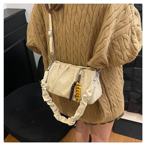 Detail of beige pleated cloud bag featuring wooden bead charm and suede-like texture
