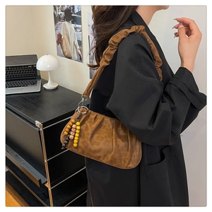 Detail of retro brown pleated shoulder bag with scrunchie strap and bead charm