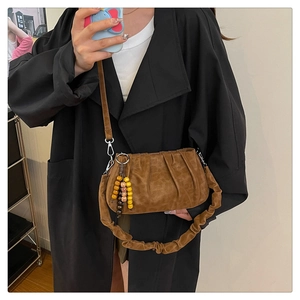 Close-up of brown pleated dumpling bag featuring wooden bead charm and ruched handle