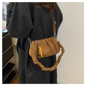 Detail of a brown ruched cloud bag with wooden bead pendant and crossbody strap