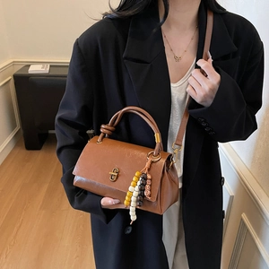 Vintage brown leather crossbody bag with beaded tassel charm on elegant black blazer