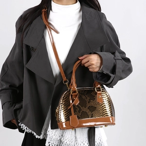Brown snake-print shell handbag with shiny finish and gold hardware shown on a model