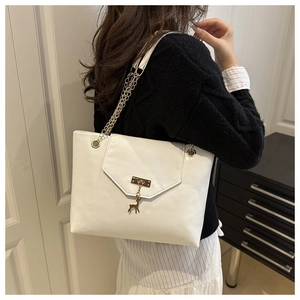 Detailed view of white tote bag with envelope flap, gold buckle, and deer charm