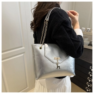 Detail of silver metallic tote bag with chain strap and gold deer pendant on model