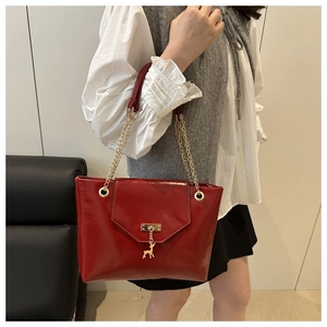 Detail of red glossy leather shoulder bag featuring a gold deer charm and chain strap