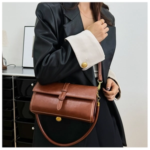 Dettaglio di una borsa a tracolla in pelle marrone con fibbia dorata su un modello