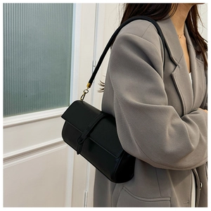 Dettaglio di borsa a tracolla in pelle nera con finiture in bronzo su blazer grigio