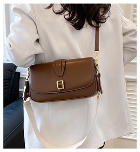 Detail of a brown leather crossbody bag with gold buckle and stylish wide fabric strap