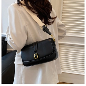 Detail of a black leather crossbody bag with gold buckle and wide woven shoulder strap