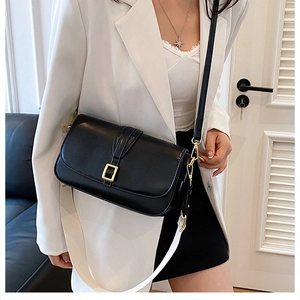 Detail showing black minimalist crossbody bag with wide strap and gold buckle hardware
