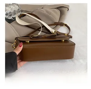 Detail of wear-resistant gold metal feet on the bottom of a brown leather crossbody bag