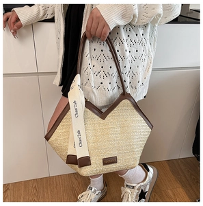 Detail view of woven straw tote bag with brown leather trim and decorative ribbon