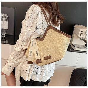 Detail of a beige straw tote bag with brown leather handles and decorative ribbon