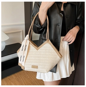 Close-up of a woven straw tote with leather handles and decorative silk scarf detail