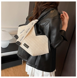 Detail of straw woven tote bag with contrast black trim and branded fabric shoulder strap