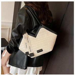 Detail of a large woven straw tote bag with black leather trim and decorative ribbon
