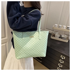 Détail du cabas monogramme vert clair avec logo doré porté par un mannequin pour le travail