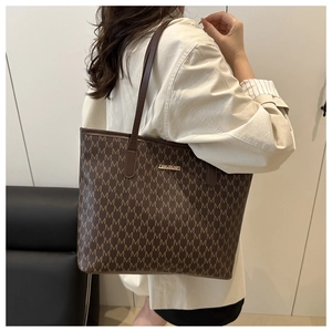 Vue détaillée d'un grand sac cabas marron à motifs M porté à l'épaule par un mannequin