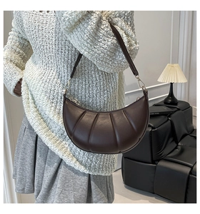 Detail of dark brown leather crescent bag with vertical pleats and golden round hardware