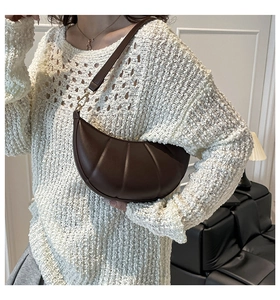 Close-up of deep brown pleated crescent bag with gold buckles on a stylish model