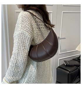 Detail of dark brown crescent bag with quilted wave texture and gold hardware on shoulder