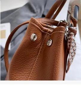 Close-up of brown litchi leather bucket bag with silver studs and patterned silk scarf