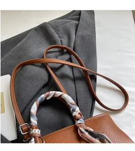 Detail of a brown lychee pattern handbag with a stylish silk scarf wrapped around the handle
