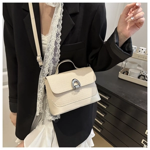Detail of off-white tote bag featuring woven texture flap and horseshoe metal buckle
