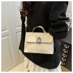 Close-up of minimalist beige crossbody bag with woven texture lid and silver metal lock
