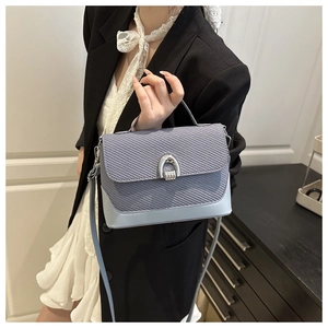 Detail of light blue handbag featuring woven flap texture and silver horseshoe lock buckle