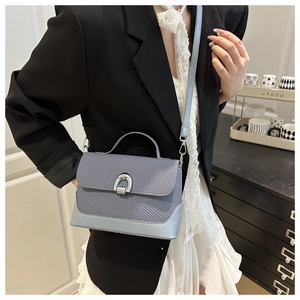 Detail of blue woven handbag showing silver arch swivel lock and smooth leather base