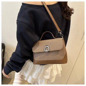 Detailed view of brown woven crossbody bag with metallic horseshoe buckle worn by model
