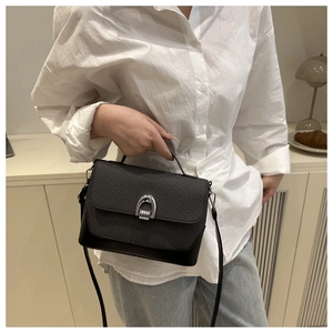 Détail d'un sac noir à texture tressée avec boucle fer à cheval argentée porté par un modèle