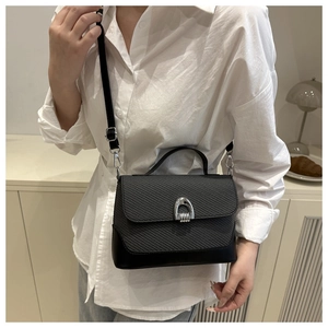 Detail of black woven shoulder bag with silver horseshoe buckle and adjustable leather strap