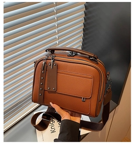 Close-up of brown litchi grain leather bag featuring double zippers and wide fabric strap