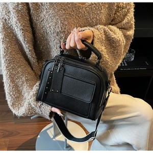 Detail of black lychee grain leather handbag with stud rivets and wide fabric strap