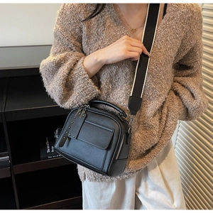 Close-up of black litchi grain leather bag with contrast wide strap and rivet details