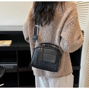 Detail of black lychee grain leather handbag with rivet tassel and wide textile strap