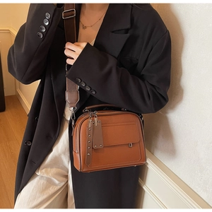 Brown lychee-textured crossbody bag detail with adjustable wide strap on black blazer