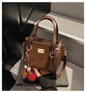 Detail of a brown suede bucket bag with gold logo plaque and plush bead pendant