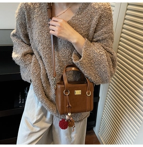 Close-up of brown bucket bag showing pebbled leather texture and retro pompom charm