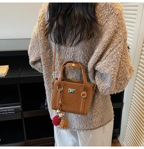 Detail of a brown faux suede bucket bag with round handles and plush ball charms